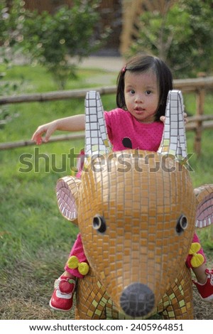 Photograph the cute expression of the little girl playing while sitting on the deer-shaped decoration