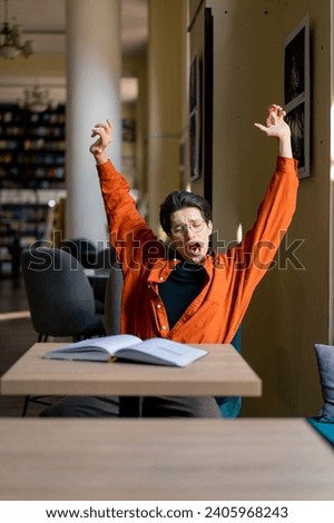 tired boy student sitting in front of a book in the library bored and yawning while preparing university exams