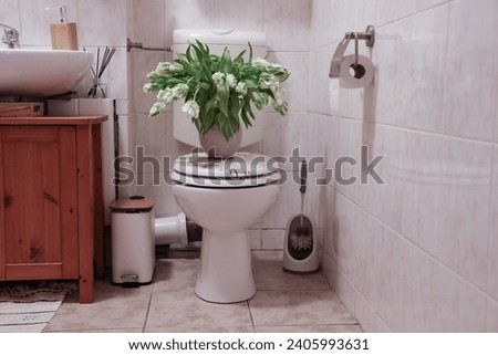 a large fresh bouquet of tulips stands in a vase on the toilet