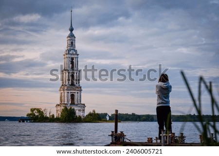 Tourist girl picturing the flooded bell tower in Kalyazin, Tver region of Russia