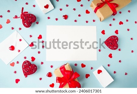Blue background, flat lay for Valentine's Day holiday, copy space for text, holiday gifts frame, envelope and red hearts, white sheet of paper.  Concept of love, romance, close relationships