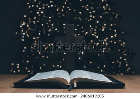 The open book of the Holy Bible. On the background is a Christmas tree. Prayer. Christmas and New Year. The birth of Jesus. Agape Crucifixion cross.