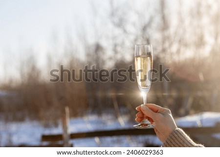 A raised glass of champagne in honor of the New Year. In hand there is a glass of champagne on a blurred winter background.