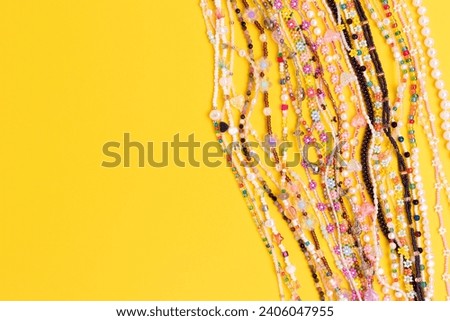 Various chains of beads, pearls and natural stones on a yellow background. Place for text.