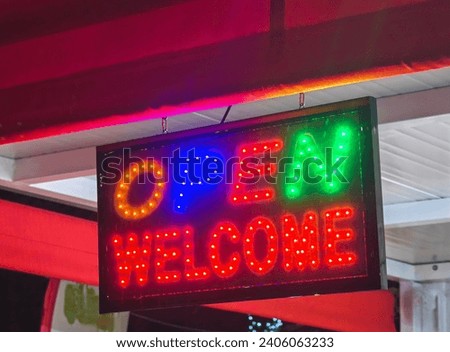 Open welcome, neon lights , store shop. Colorful sign, symbols. Orange, blue , red and green. Night time. 