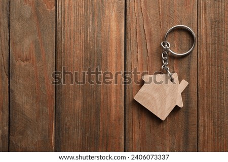 One keychain in shape of house on wooden table, top view. Space for text