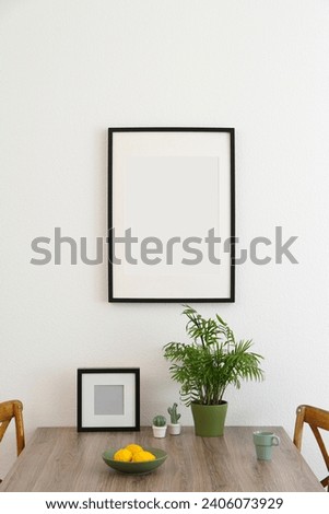 Room interior with dining table, wooden chairs and photo frames on white wall