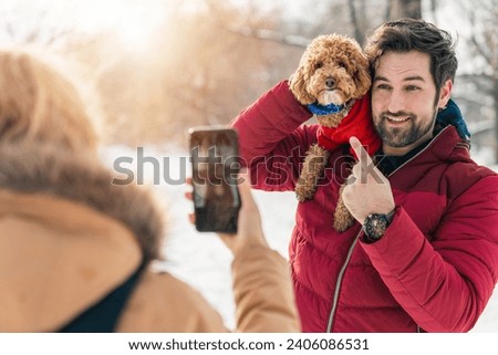 Woman taking pictures of her husband and dog while spending time outdoors. Man posing for a photo with poodle dog.