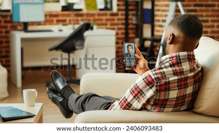 Man checking up on abroad living friend during video conference meeting over the internet. African american mates enjoying time together in online video call session while at home Royalty-Free Stock Photo #2406093483