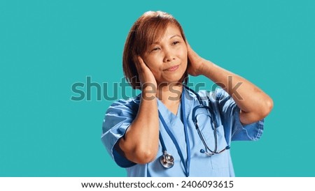 Competent nurse tormented by extreme noise while at work, close up. Healthcare employee covering ears with hands, bothered by rowdy surrounding sounds, isolated over studio background