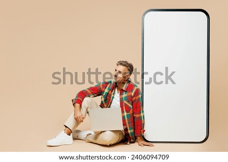 Full body minded adult man he wear red shirt white t-shirt casual clothes sit near big huge blank screen mobile cell phone smartphone with area isolated on plain pastel light beige color background