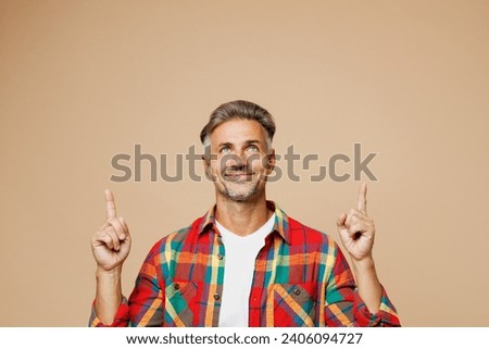 Adult happy fun man he wear red shirt white t-shirt casual clothes point index finger overhead on area mock up isolated on plain pastel light beige color background studio portrait. Lifestyle concept
