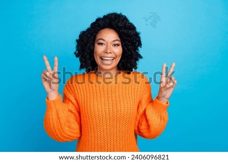 Photo portrait of attractive young woman show double v-sign excited wear trendy knitwear orange clothes isolated on blue color background