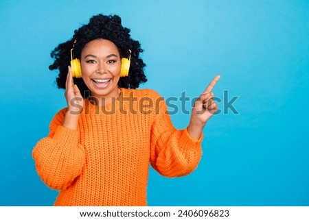 Photo portrait of lovely young lady headphones point empty space dressed stylish knitted orange garment isolated on blue color background