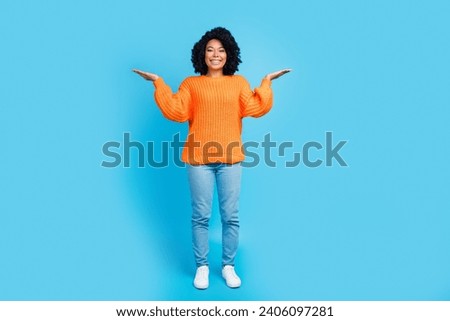 Full size photo of attractive young woman hold compare empty space wear trendy knitwear orange clothes isolated on blue color background