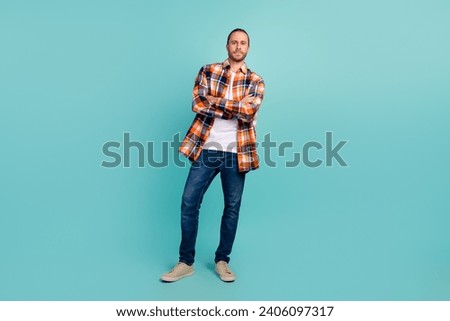 Full size photo of cool brutal man dressed checkered shirt denim pants standing holding arms crossed isolated on teal color background
