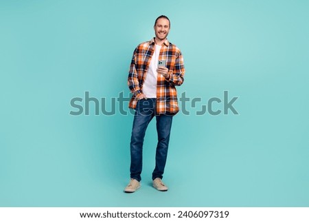 Full size photo of intelligent positive man dressed checkered shirt holding smartphone hand in pocket isolated on teal color background
