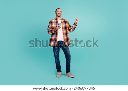 Full size photo of cool man dressed checkered shirt hold smartphone look directing at empty space sale isolated on teal color background