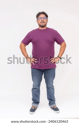 A pensive chubby man wearing glasses looking very serious, hands on hips, no nonsense mood. Full body photo, isolated on a white background. Royalty-Free Stock Photo #2406120463