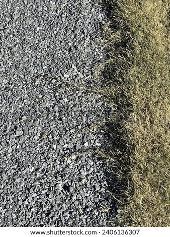 a photography of a patch of grass next to a gravel road.