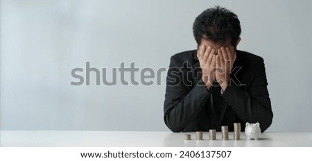 Businessman covers his face with his hands against a stack of coins, perspective on planning mistakes Stressed about finances, not saving, losing money, going bankrupt. Copy space, banner, panorama Royalty-Free Stock Photo #2406137507