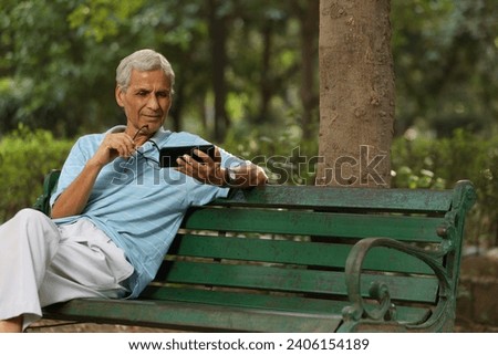 Old man using mobile  phone at the park. Senior man watching video in phone. Aging man reading online news through mobile phone.