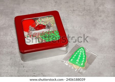 Homemade sugar cookies with royal icing packaged in a square tin gift box with window lid.