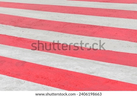 It is zebra crossing with red and white rows. It is close up view of red zebra in sunny day.