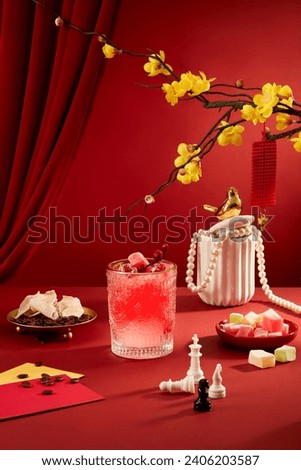 A striking glass of juice takes center stage on a red background, complemented by seahorse chess pieces, dried jam, and yellow apricot blossoms-a festive Tet party table focal point. Royalty-Free Stock Photo #2406203587