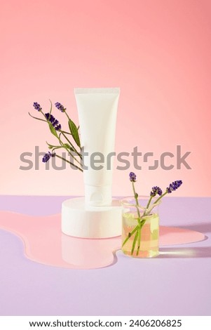 Close-up of an unlabeled cosmetic tube displayed on a white podium, surrounded by lavender flowers. Pastel pink and purple background. Scene for cosmetics advertising. Royalty-Free Stock Photo #2406206825