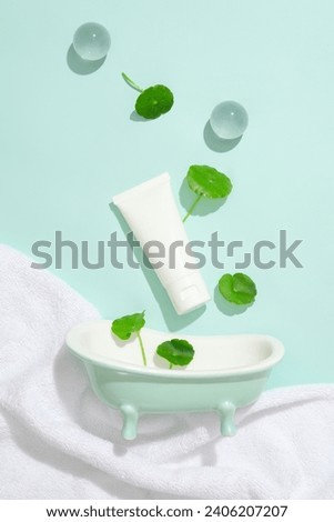 A tube of unlabeled lotion, two glass balls, a mini bathtub and pennywort leaves on pastel background. Gotu kola contains anti-inflammatory and antibacterial compounds.