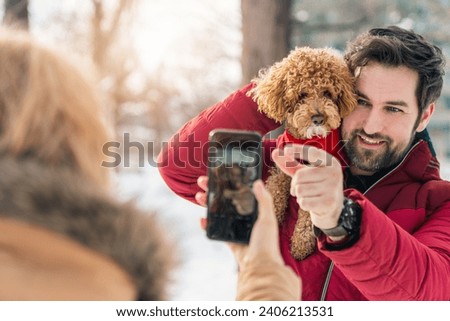 Adult couple taking picture with poodle dog outdoors. Woman photographing with mobile phone man and dog poodle together while enjoying the day outdoors.