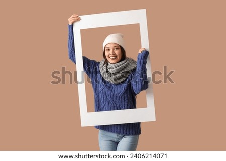 Beautiful young Asian woman in warm scarf with frame on brown background