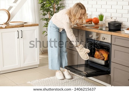 Beautiful young woman taking tasty baked turkey from oven in kitchen. Thanksgiving Day celebration Royalty-Free Stock Photo #2406215637