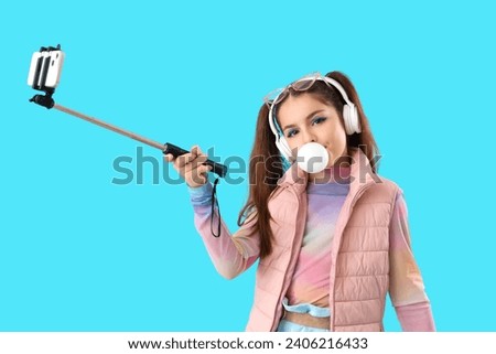Trendy girl blowing bubble gum and taking selfie on blue background