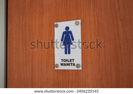 A women's toilet sign on a wooden door in a public toilet.
The text on the sign with the words "TOILET WANITA" means "WOMEN'S TOILET"