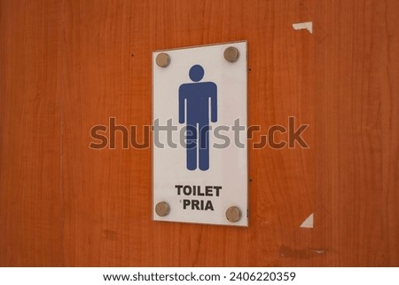 The wooden door of the public toilet has a men's toilet sign posted on it.
The text on the sign with the words "TOILET PRIA" means "MEN'S TOILET"