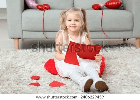 Cute little girl cutting paper hearts in room decorated for Valentines Day Royalty-Free Stock Photo #2406229459