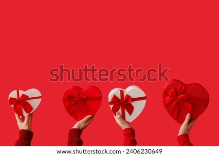 Female hands holding heart-shaped gift boxes on red background. Valentine's Day celebration