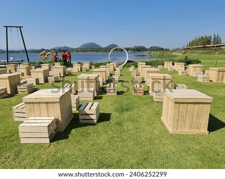 Crate or light wood is arranged with tables and chairs to create a beer garden on the background of a bright green lawn.  Royalty-Free Stock Photo #2406252299