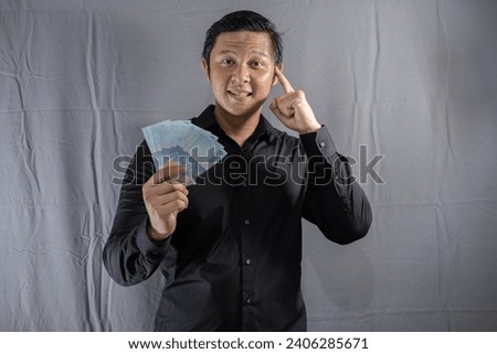 Young Asian businessman holding money with a happy gesture because his business and finances are on the rise