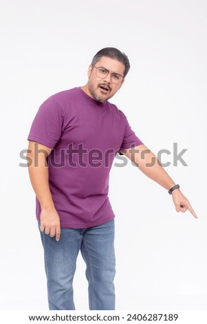 A middle aged man looking puzzled and befuddled while pointing to something below to the right, 45 degree angle. Full body photo, isolated on a white background. Royalty-Free Stock Photo #2406287189