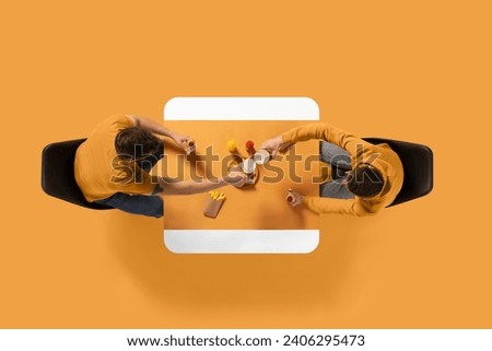 Creative collage. young attractive man sitting at common table and eating fast food and drinking beer against yellow background. Copy space. Concept of business lunch, morning meeting, briefing. Royalty-Free Stock Photo #2406295473