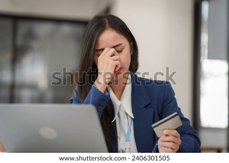 stressed young businesswoman with a credit card in hand, looking worried in front of her laptop.