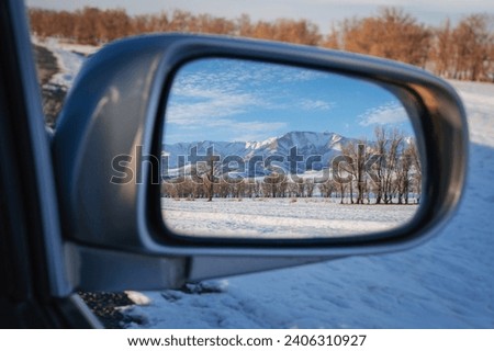 reflection of winter landscape with Tien Shan mountains and trees in field in snow in rearview mirror of the car. Concept of festive winter travel in Kazakhstan