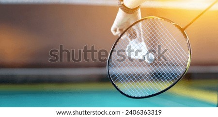 Badminton player holds racket and white cream shuttlecock in front of the net before serving it to another side of the court, soft focus, lens flare edited, copy space.