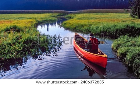 A man in a red canoe in Hosmer Lake in the Oregon Cascae mountains near Bend Royalty-Free Stock Photo #2406372835