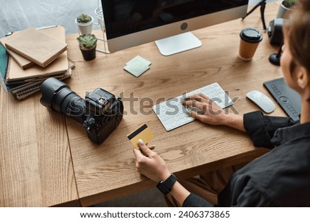 cropped view of young female photographer sitting at table using credit card to pay online