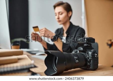 focus on camera on table next to young blurred female photographer paying online with credit card