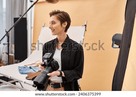 cheerful beautiful female photographer in everyday clothing working with her equipment at studio